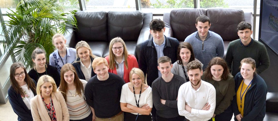 An overhead shot of some of the students and graduates on the Dawn Farms placement programme smile up at the camera.