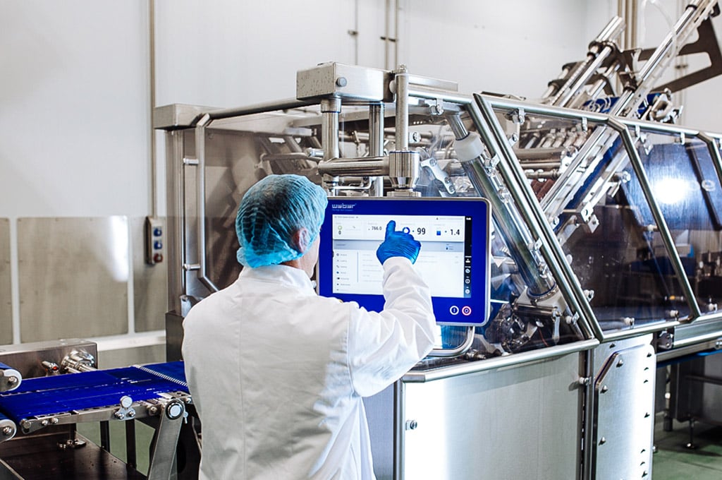 A man in a white coat and blue hairnet supervises a high-tech touchscreen device in the Dawn Farms state-of-the-art processing facilities.
