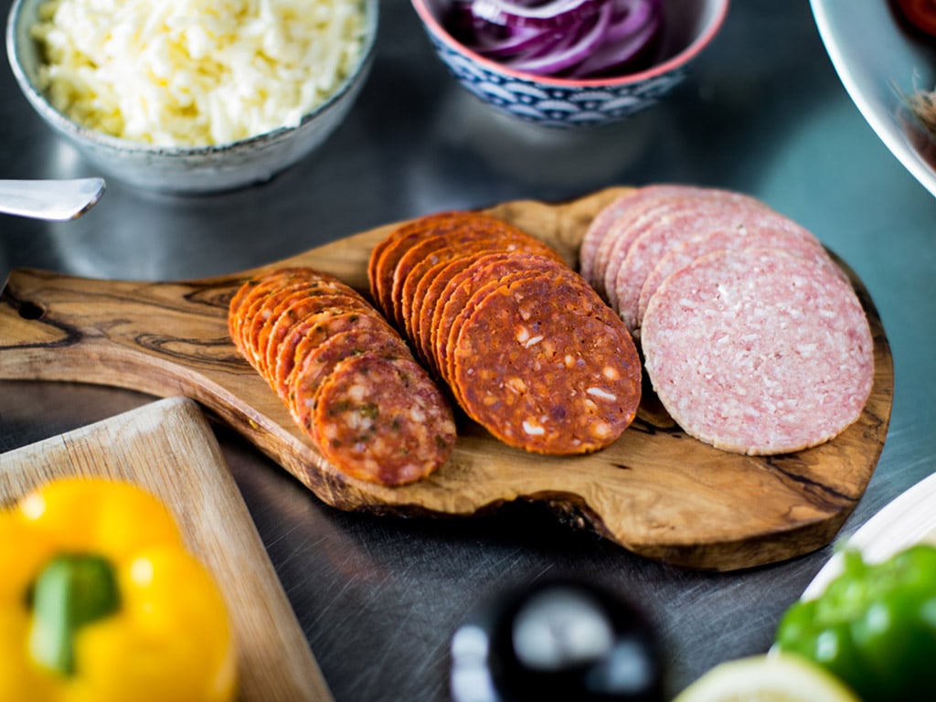 A selection of Dawn Farms cured and fermented meat slices - including chorizo and pepperoni - are arrayed on a wooden platter.