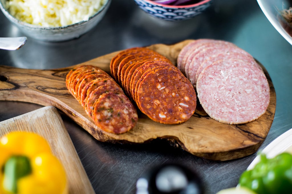 A selection of Dawn Farms sliced, fermented meat products - chorizo, pepperoni, salami – displayed on a wooden serving board.