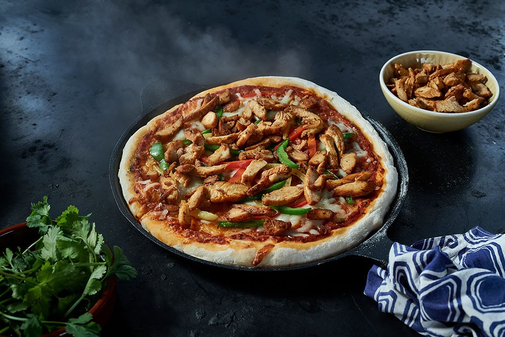 An iron pan containing an oven-baked cheese pizza topped with Dawn Farms Batch 85 fajita chicken and red and green peppers.