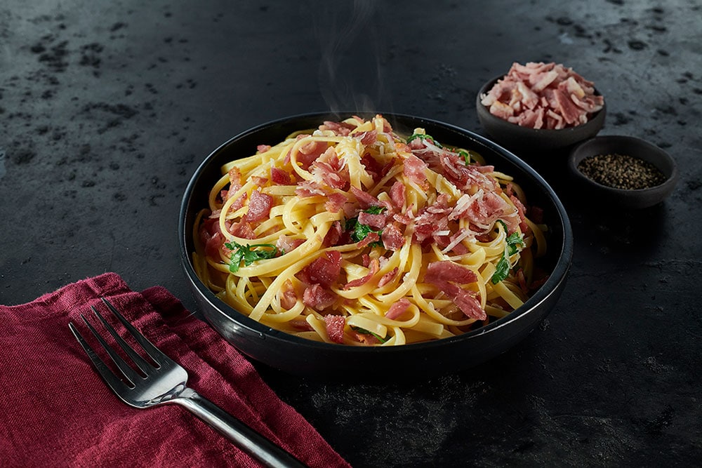 A bowl of classic steaming, spaghetti carbonara using tasty Dawn Farms Batch 85 bacon pieces.