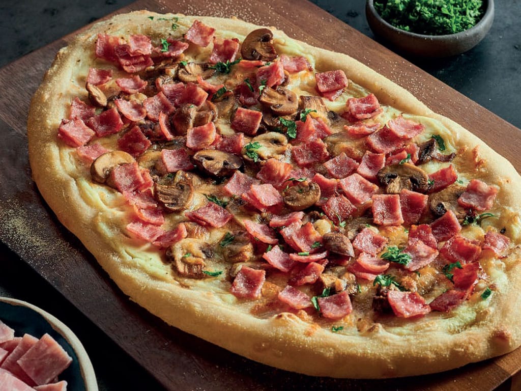 A large, cooked flatbread pizza scattered with Habibi Halal turkey stamps and sliced mushrooms.